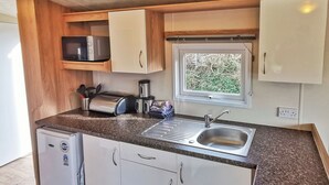 A compact kitchenette with a sink, a microwave, a toaster, and a small refrigerator. - Spacious and well presented 12ft wide caravan with one double and two twin. (Ludchurch, Nr Saundersfoot)
