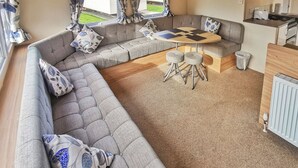 A caravan interior with a sofa set, a dining table, and a kitchen area. - Spacious and well presented 12ft wide caravan with one double and two twin. (Ludchurch, Nr Saundersfoot)