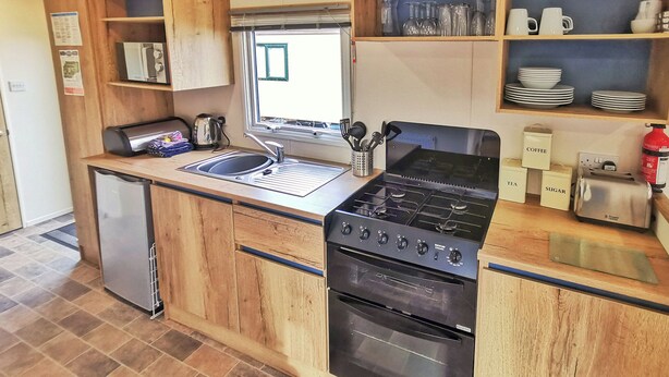 A compact kitchen with a sink, stove, oven, and wooden cabinets. - Spacious and well presented 12ft wide caravan with one double and two twin. (Ludchurch, Nr Saundersfoot)
