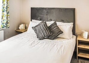 A neatly made bed with white linens, striped pillows, and a dark headboard. There are bedside tables with lamps and a framed picture.