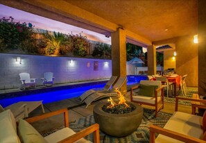 Un área junto a la piscina con sillones reclinables, una fogata y una zona de comedor.
