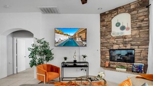 A living room with a stone fireplace, a flat-screen TV, a sofa, a coffee table, and a potted plant. - The Desert Gem Pool Spa Gated Private Home (Desert Hot Springs)