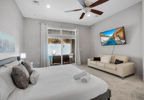 Una habitación de hotel con cama, sofá, televisión y ventilador de techo.