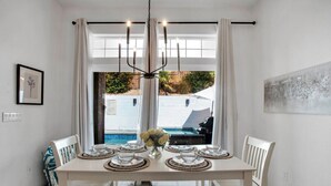 A dining area with a table set for four, a chandelier, and a view of a pool and outdoor area. - The Desert Gem Pool Spa Gated Private Home (Desert Hot Springs)