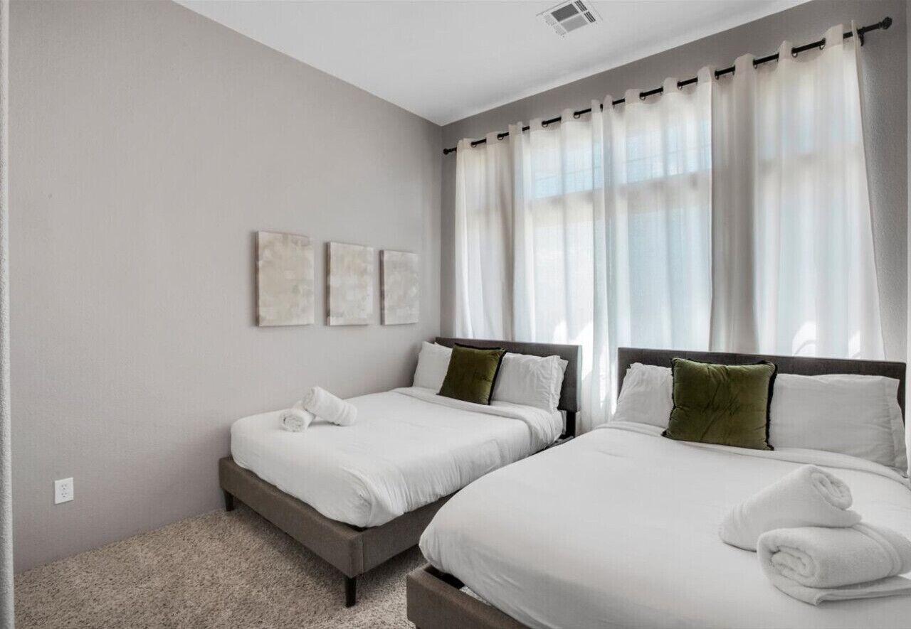 A hotel room with two beds, a large window with sheer curtains, and a neutral color scheme.