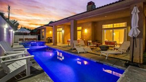 A swimming pool with lounge chairs, a covered seating area, and a sunset sky. - The Desert Gem Pool Spa Gated Private Home (Desert Hot Springs)