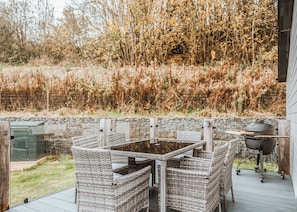 Une terrasse extérieure avec des meubles en osier, une table en verre et un barbecue.