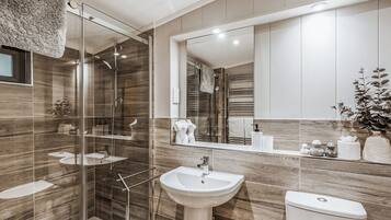 A modern bathroom with a glass shower enclosure, a pedestal sink, and a large mirror.