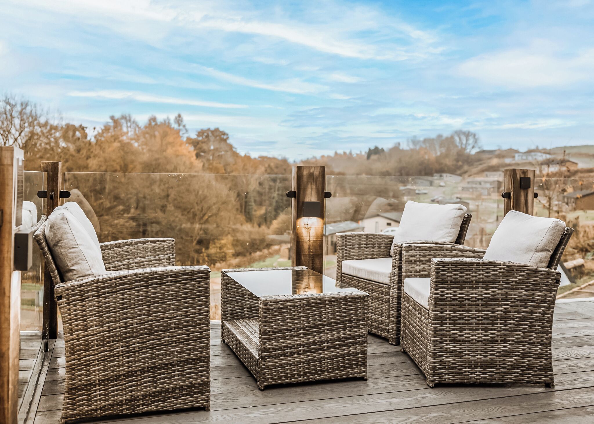 A wicker outdoor seating area with a glass table and chairs, overlooking a scenic landscape.