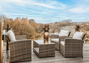 Un espacio de estar al aire libre con muebles de mimbre, una mesa y sillas de vidrio, con vistas a un paisaje pintoresco.