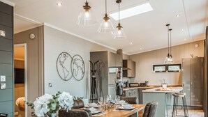 Een moderne keuken met een centraal eiland, hanglampen en een eethoek met een houten tafel en stoelen.