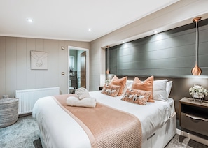 Une chambre moderne avec un grand lit, une table de chevet, un radiateur et une vue sur la salle de bain.