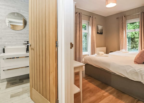 Ein Schlafzimmer mit Bett, Nachttisch, einem Fenster mit Vorhängen, einer Heizung und einem Spiegel an der Wand.