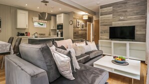 A modern living room with a grey sectional sofa, a flat-screen TV, and a dining area with a kitchen in the background.