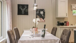 A dining table set with chairs, a chandelier, a potted orchid, a champagne bottle, and a painting of a deer head.