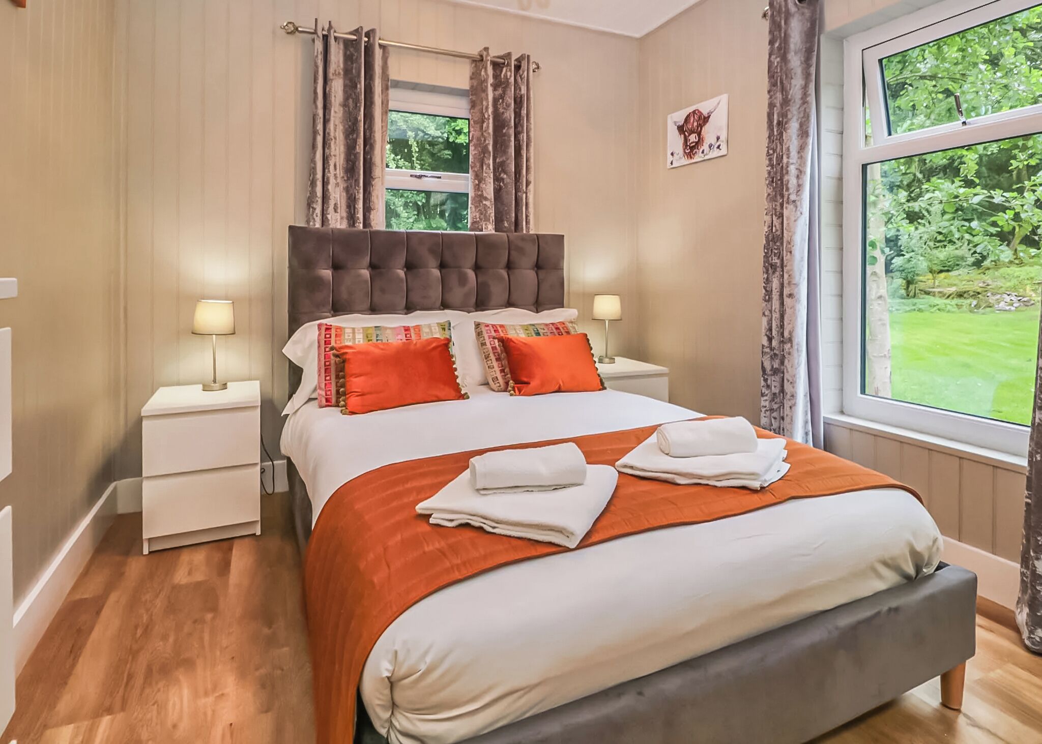 A bedroom with a large bed, two bedside tables with lamps, a window with curtains, and a picture on the wall.