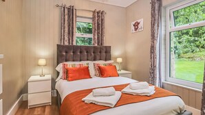 A bedroom with a large bed, two bedside tables with lamps, a window with curtains, and a picture on the wall.