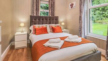 A bedroom with a large bed, two bedside tables with lamps, a window with curtains, and a picture on the wall.