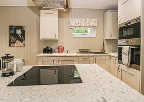 A modern kitchen with a central island, built-in oven, and a window with a view. - Deluxe lodge with one master double with an en suite shower and one twin. (Cartmel)