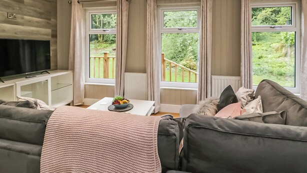 A living room with a sofa, a TV, and windows with curtains.