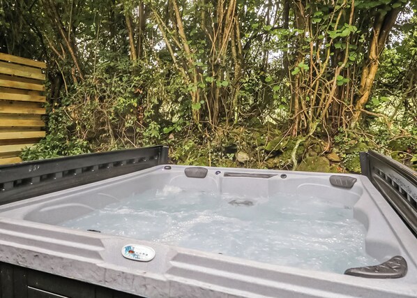 A hot tub with a wooden bench, surrounded by dense foliage. - Deluxe lodge with one master double with an en suite shower and one twin. (Cartmel)