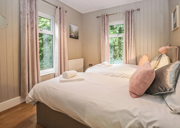 A double bed with a rolled towel, a bedside lamp, and a view of greenery through the window. - Deluxe lodge with one master double with an en suite shower and one twin. (Cartmel)