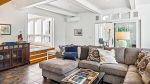 Ein geräumiges Wohnzimmer mit einem Ecksofa, einem Holzschrank und einem großen Fenster, das für natürliches Licht sorgt.