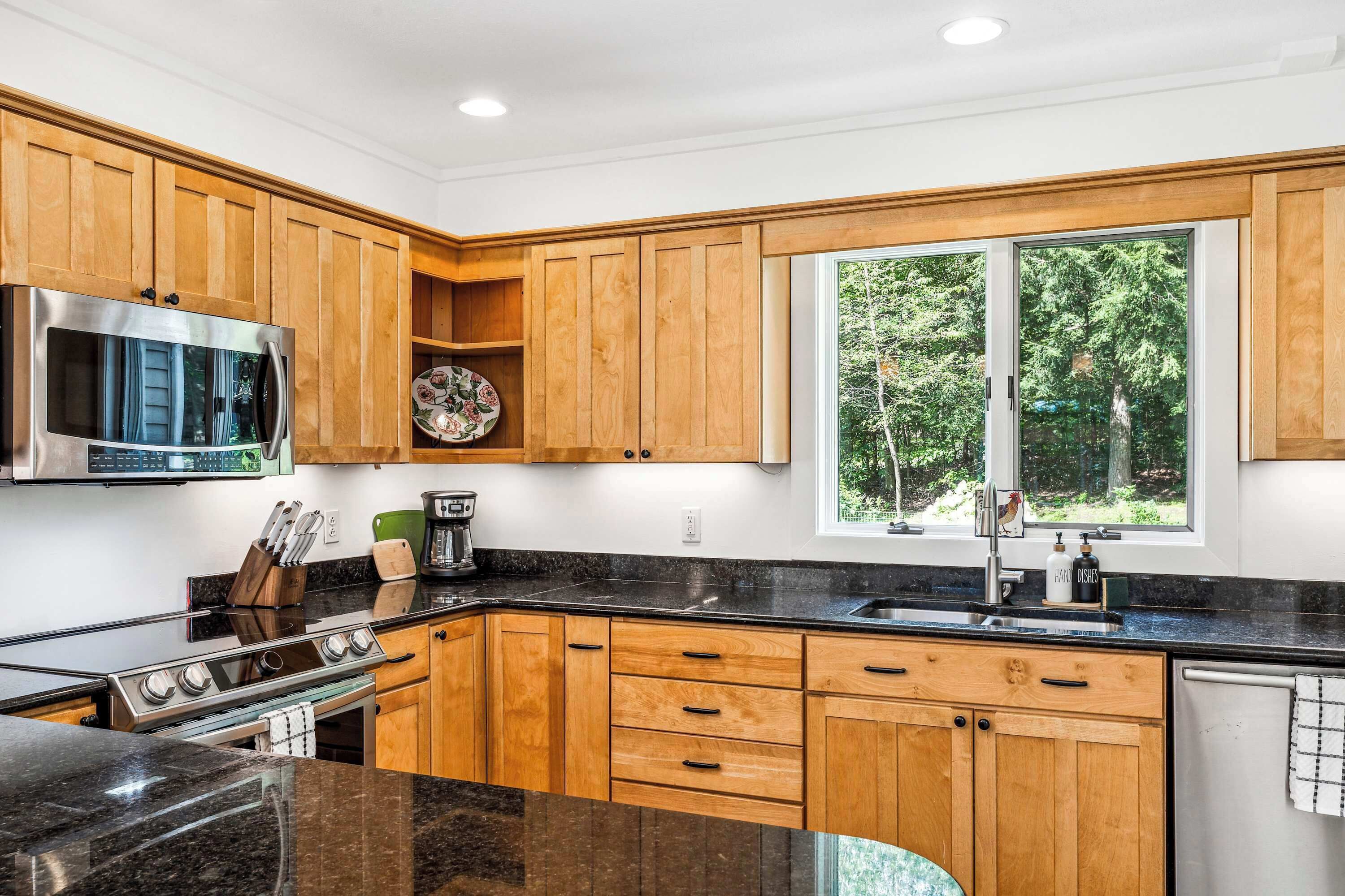A modern kitchen with wooden cabinets, a stainless steel stove, and a large window with a view of trees.