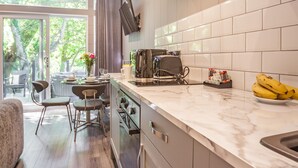 A modern kitchen with a large window, a dining area with chairs, and a countertop with a toaster and bananas.