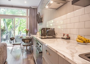 A modern kitchen with a large window, a dining area with chairs, and a countertop with a toaster and bananas. - 2 bedroom accommodation in Snowdonia (Snowdonia)