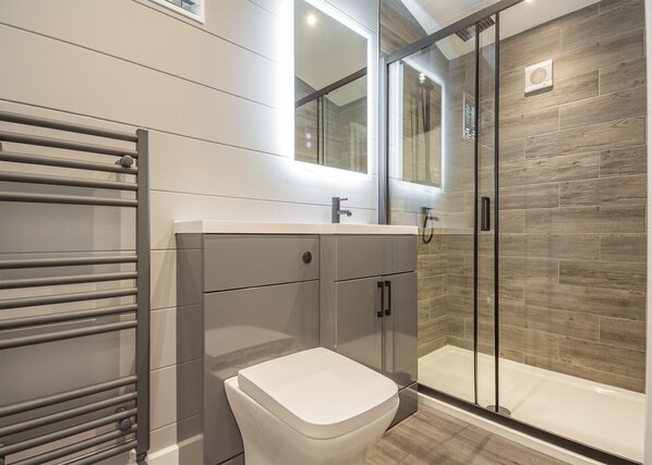 Une salle de bain moderne avec une douche à parois de verre, des toilettes blanches et un meuble-lavabo avec un miroir.