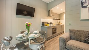 A modern kitchen with a flat-screen TV, a dining area with a glass table, and a grey sofa.