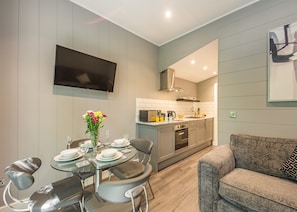 A modern kitchen with a flat-screen TV, a dining area with a glass table, and a grey sofa. - 2 bedroom accommodation in Snowdonia (Snowdonia)