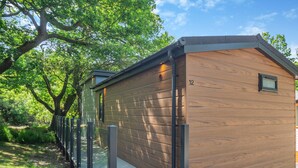 A modern wooden cabin with a metal railing, a small window, and a number '12' on the side.
