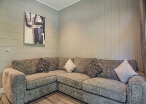 Un soggiorno angolare con un divano componibile, cuscini decorati, un quadro astratto incorniciato e pareti rivestite in legno.