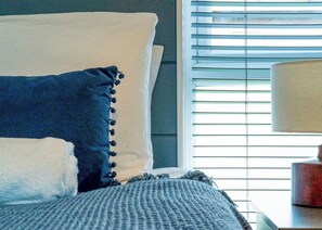 Una cama con almohadas, una lámpara y una ventana con persianas.