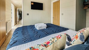 A bedroom with a bed, a TV mounted on the wall, and a wooden door. - 2 bedroom accommodation in Tewkesbury (Tewkesbury)