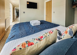 A bedroom with a bed, a TV mounted on the wall, and a wooden door.