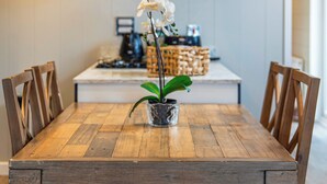 A wooden dining table with chairs, a potted orchid, and a kitchen area in the background.