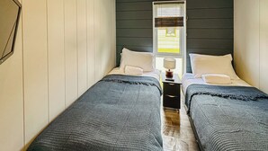 A bedroom with two beds, a nightstand with a lamp, and a window with blinds.