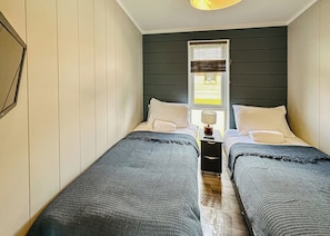 Un dormitorio con dos camas, una mesita de noche con lámpara y una ventana con persianas.