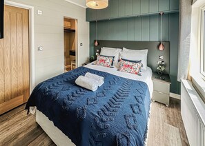 Un dormitorio con una cama, una mesita de noche, una puerta de madera y una ventana.
