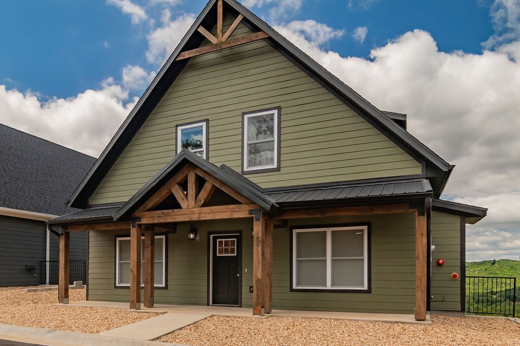 A green building with a gabled roof, two windows, and a front door.