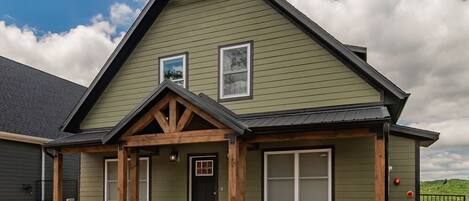 A green building with a gabled roof, two windows, and a front door.
