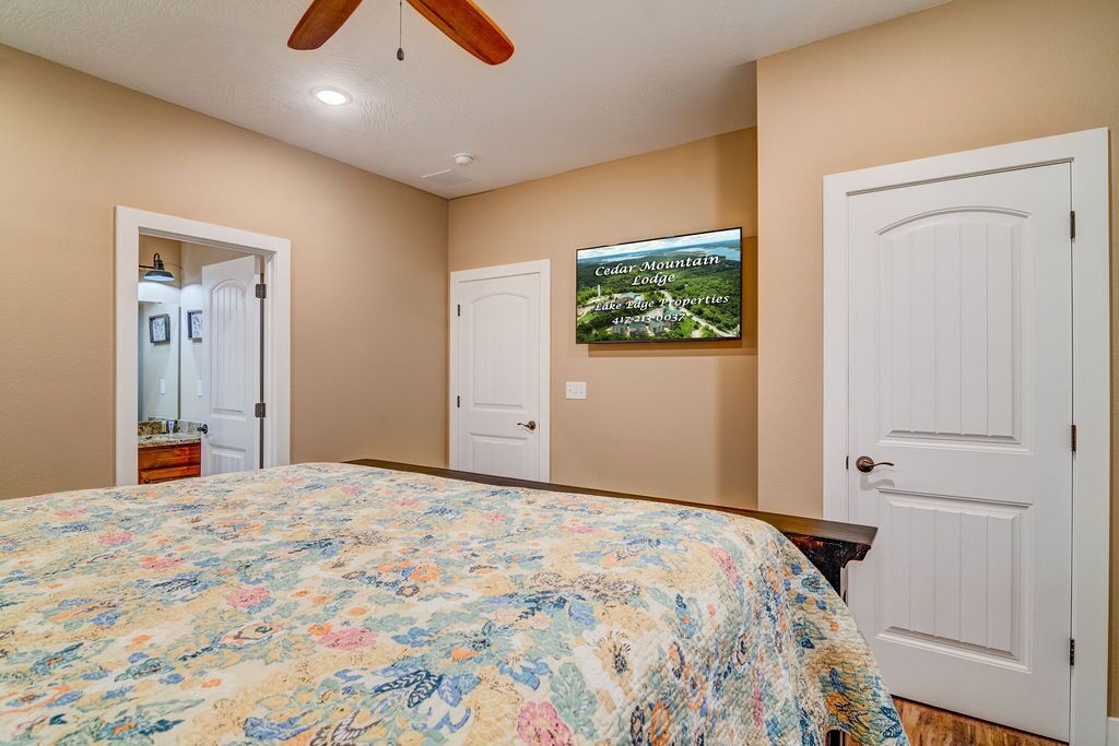 A bedroom with a floral bedspread, a ceiling fan, a framed picture on the wall, and two white doors.