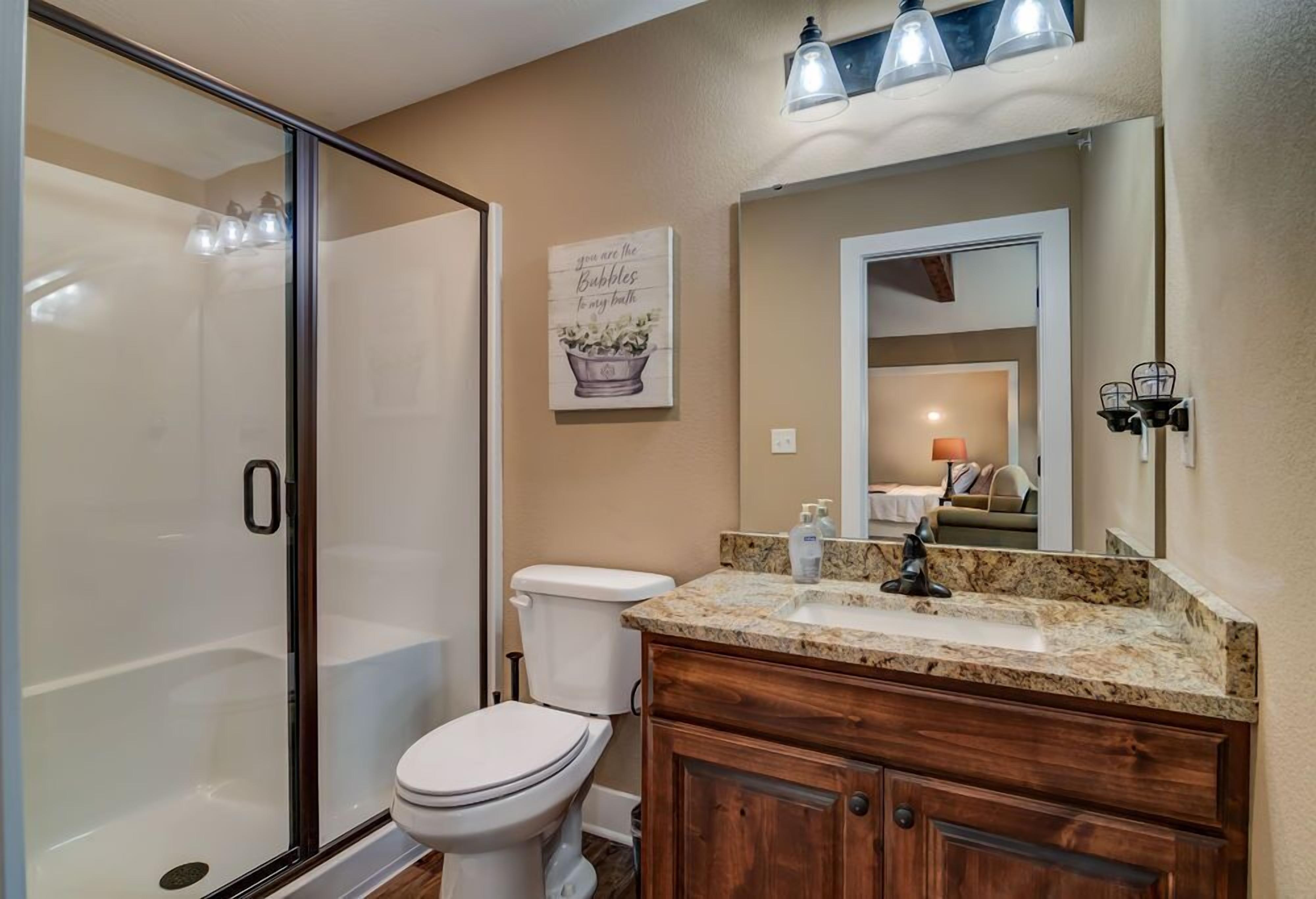 A bathroom with a glass shower enclosure, a toilet, a vanity with a sink, and a mirror.