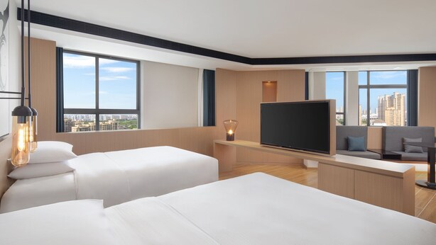 Habitación de hotel moderna con dos camas, un televisor de pantalla plana, un escritorio y un ventanal con vistas a la ciudad.