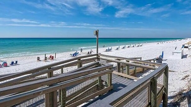 Ein Strand mit einer hölzernen Promenade, die zum Ufer führt, bewölkter Himmel und ruhiges Meer.