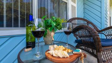 Una mesa dispuesta con copas de vino, una botella de Merlot, queso, galletas y una silla de mimbre.