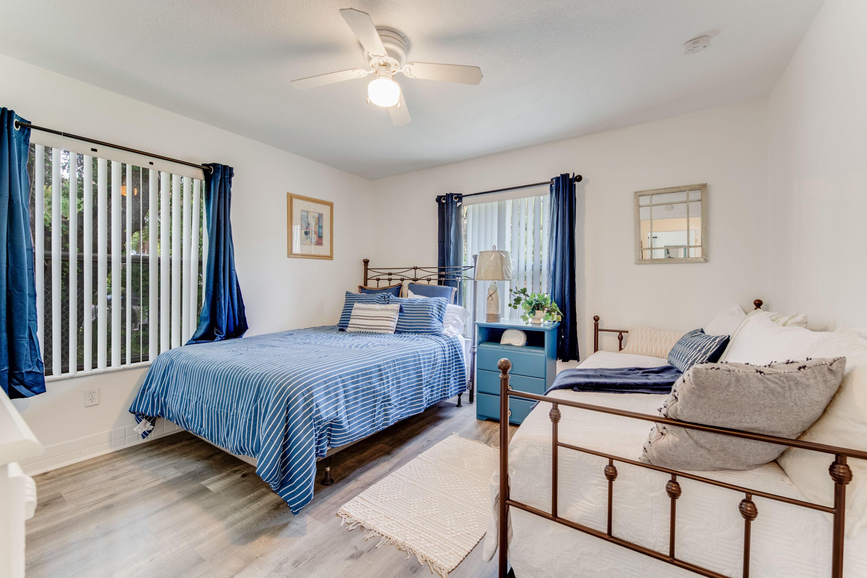 A bedroom with a bed, a nightstand, a dresser, a ceiling fan, and a window with curtains.